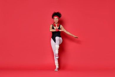 Woman with headphones doing aerobic exercise on red background