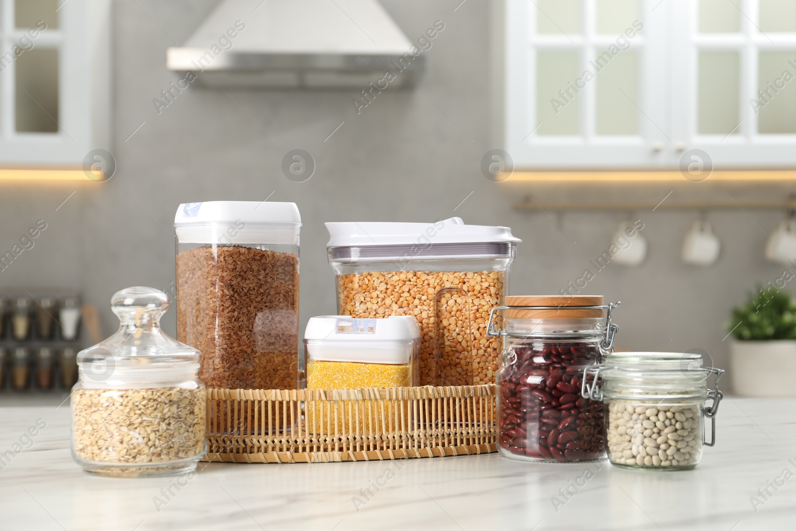 Photo of Different types of cereals and legumes in containers on white marble table in kitchen