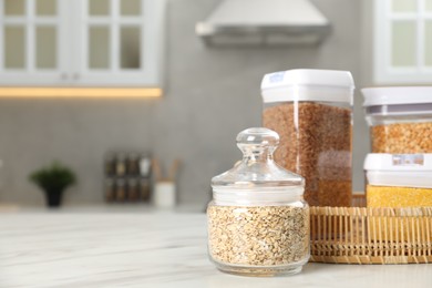 Different types of cereals in containers on white marble table in kitchen, space for text