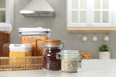 Photo of Different types of cereals and legumes in containers on white marble table in kitchen