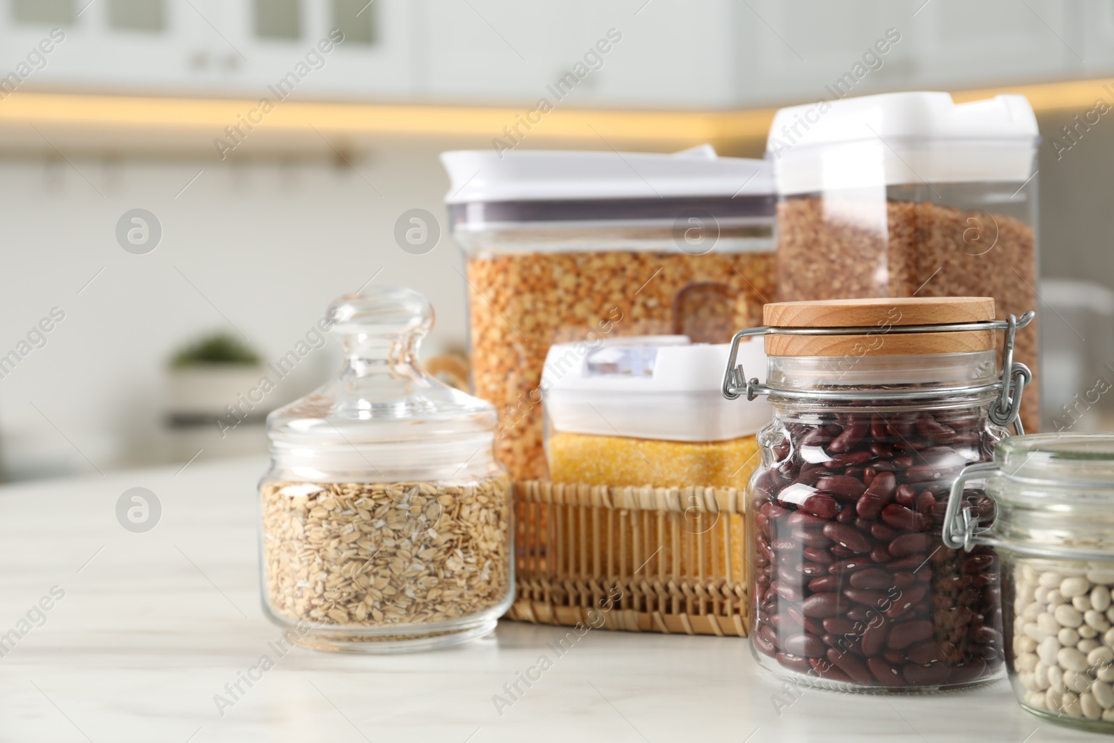 Photo of Different types of cereals and legumes in containers on white marble table in kitchen, closeup