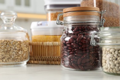 Photo of Different types of cereals and legumes in containers on white marble table in kitchen, closeup