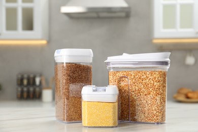 Different types of cereals in containers on white marble table in kitchen