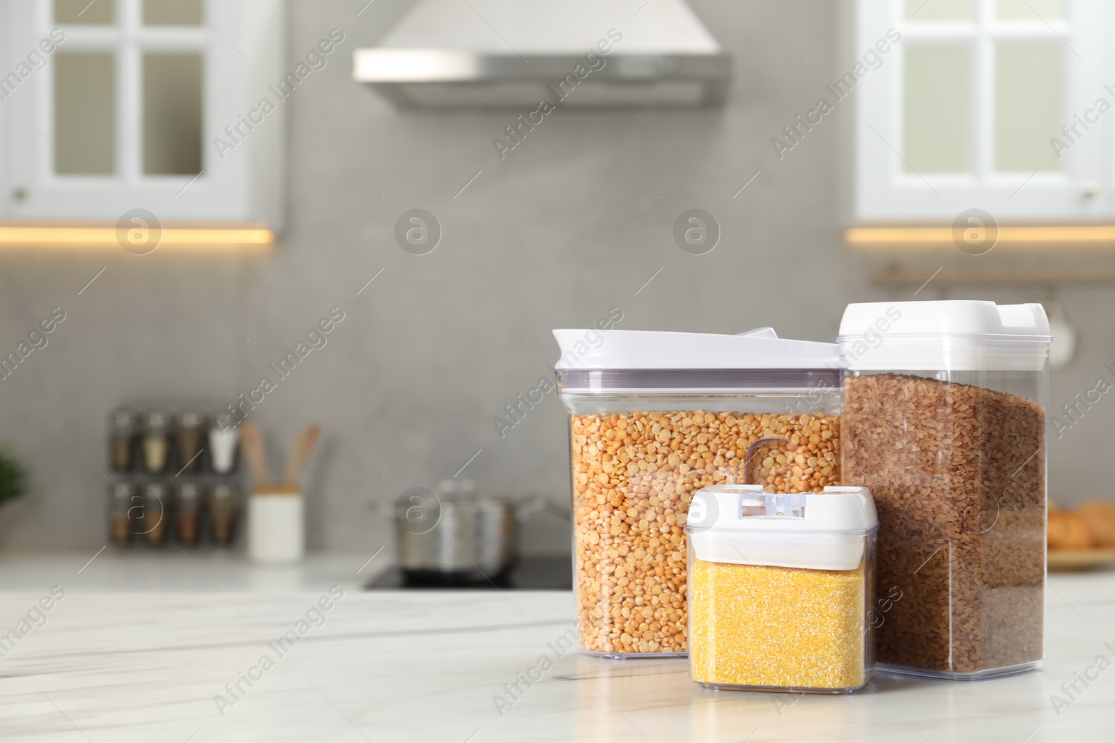 Photo of Different types of cereals in containers on white marble table in kitchen, space for text