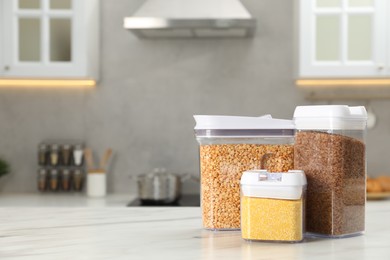 Photo of Different types of cereals in containers on white marble table in kitchen, space for text