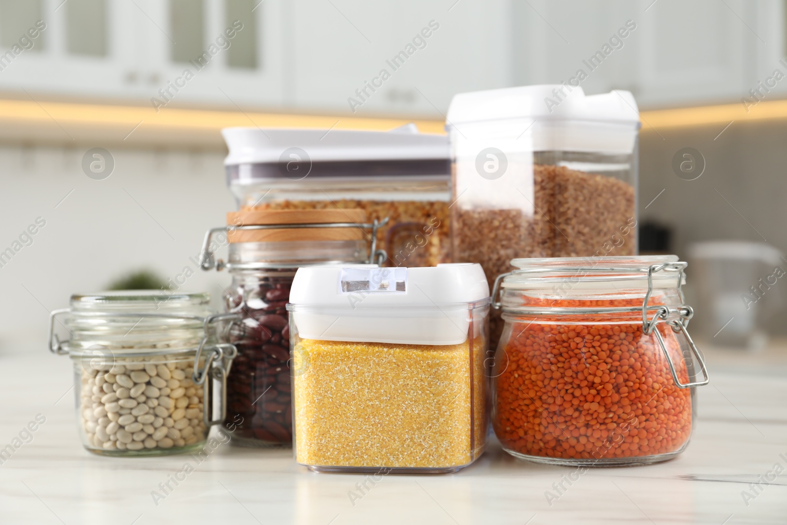 Photo of Different types of cereals and legumes in containers on white marble table in kitchen