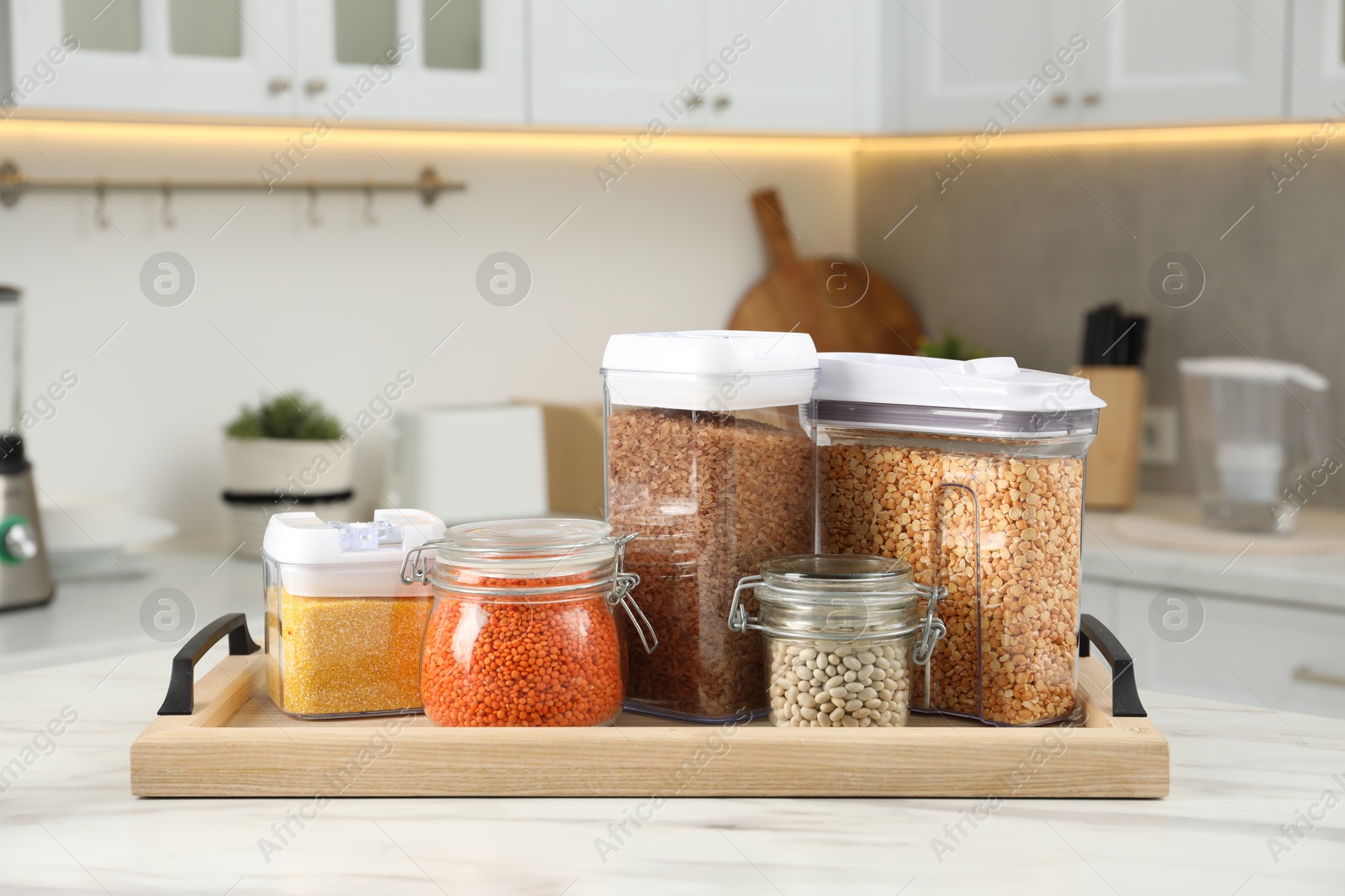 Photo of Different types of cereals and legumes in containers on white marble table in kitchen