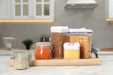 Photo of Different types of cereals and legumes in containers on white marble table in kitchen