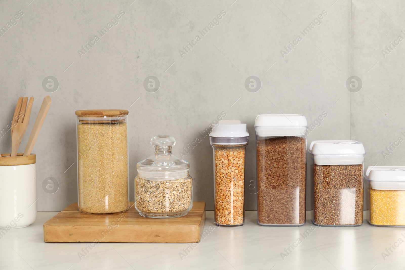 Photo of Different types of cereals and legumes in containers on white marble table in kitchen