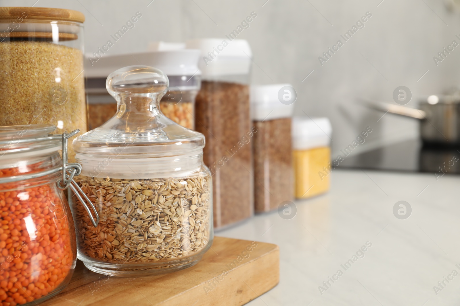 Photo of Different types of cereals and legumes in containers on light table in kitchen, closeup. Space for text