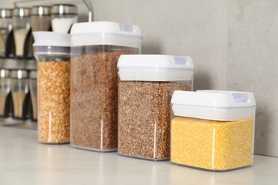 Different types of cereals and legumes in containers on light marble table, closeup