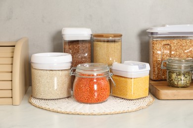 Photo of Different types of cereals, seeds and legumes in containers on light marble table