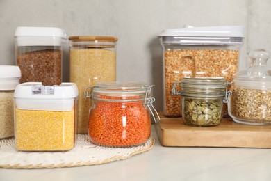 Different types of cereals, seeds and legumes in containers on light marble table