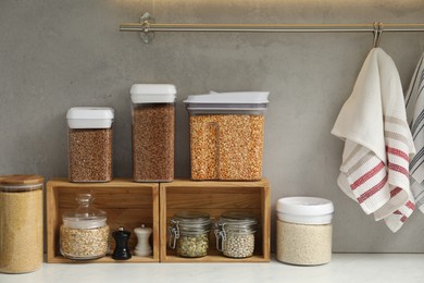 Different types of cereals, seeds and legumes in containers on light marble table