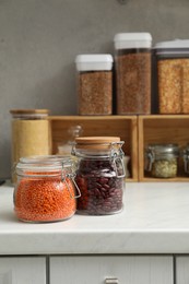 Photo of Different legumes and cereals in containers on light countertop in kitchen