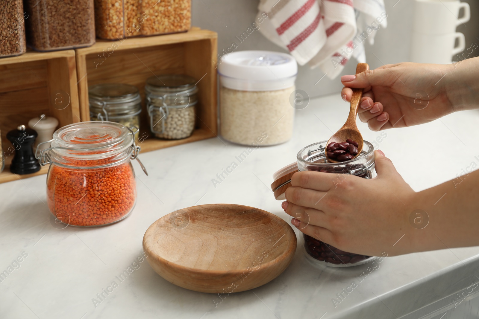 Photo of Woman putting beans from jar at light marble countertop in kitchen, closeup