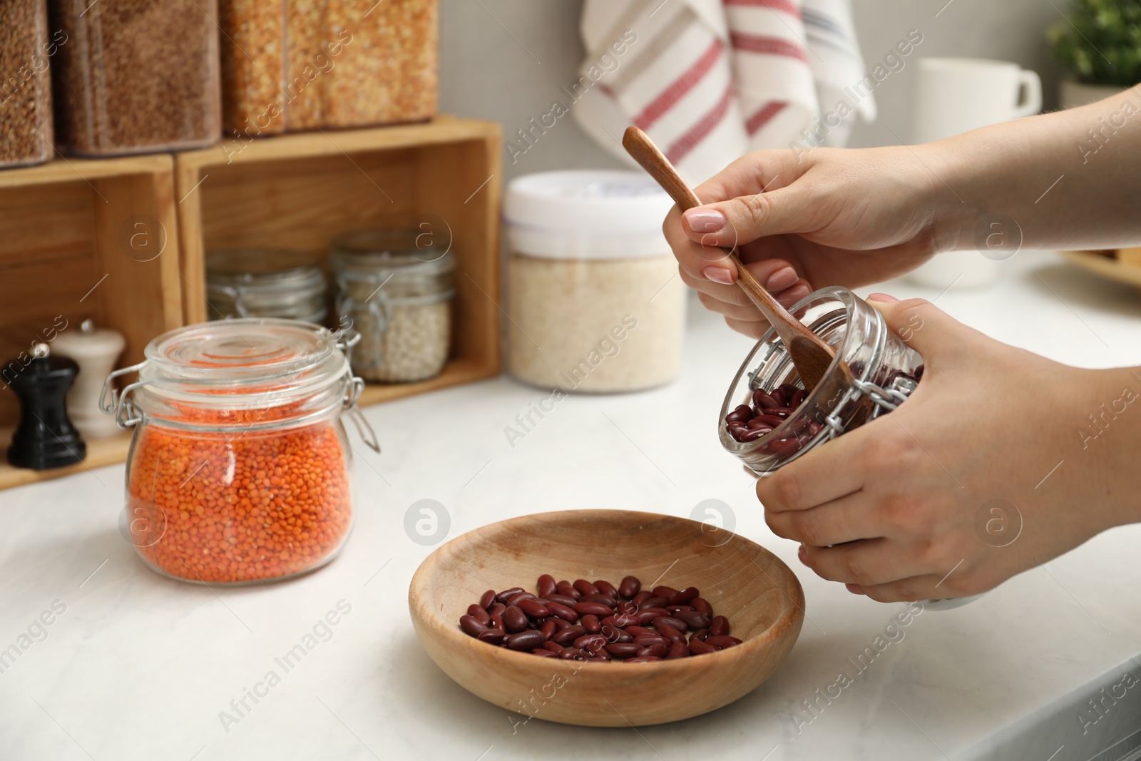 Photo of Woman putting beans from jar at light marble countertop in kitchen, closeup