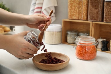 Photo of Woman putting beans from jar at light marble countertop in kitchen, closeup