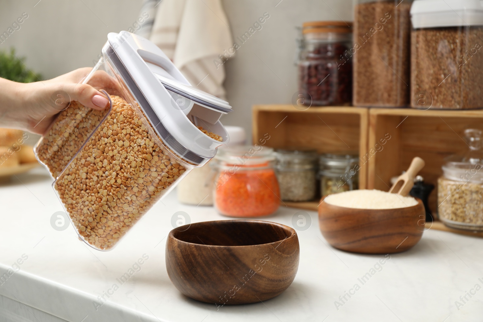 Photo of Woman putting peas from container into bowl at light marble countertop in kitchen, closeup