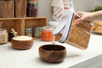 Photo of Woman putting peas from container into bowl at light marble countertop in kitchen, closeup