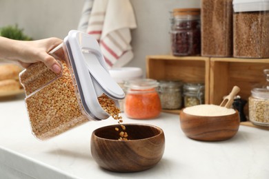 Woman putting peas from container into bowl at light marble countertop in kitchen, closeup