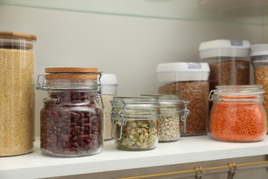 Photo of Different types of cereals, seeds and legumes in containers in closet