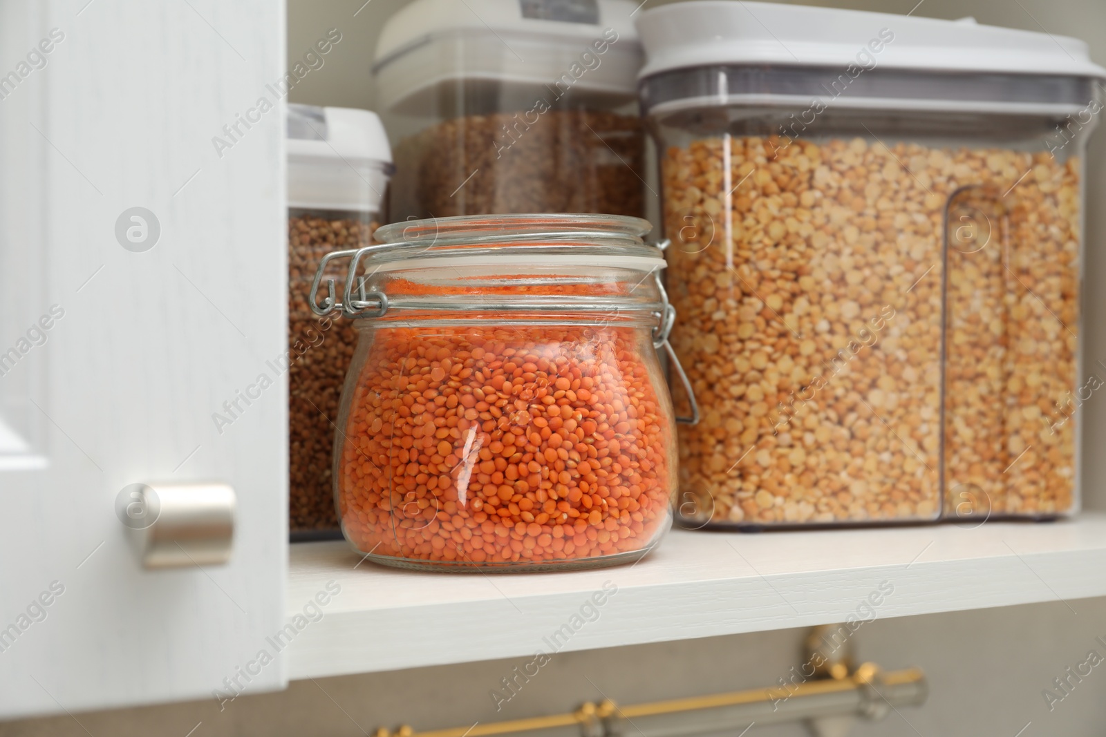 Photo of Different types of cereals and legumes in containers in closet, closeup