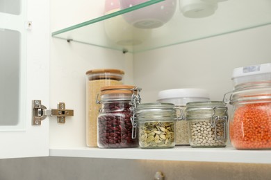 Different types of cereals, seeds and legumes in containers in closet