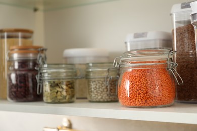 Different types of cereals and legumes in containers in closet, closeup