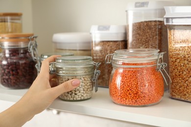 Photo of Woman with containers of different cereals and legumes in kitchen, closeup