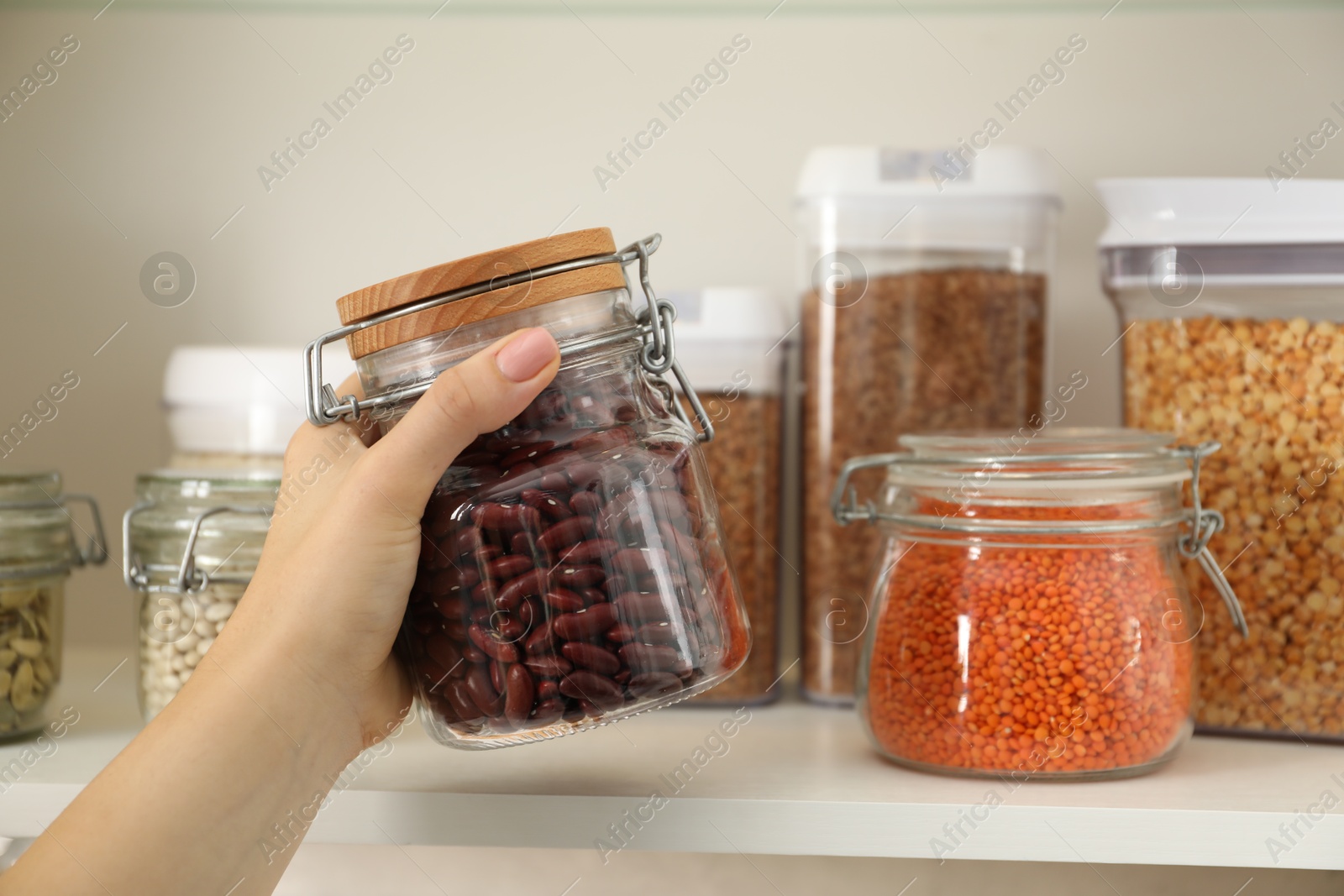 Photo of Woman with containers of different cereals and legumes in kitchen, closeup