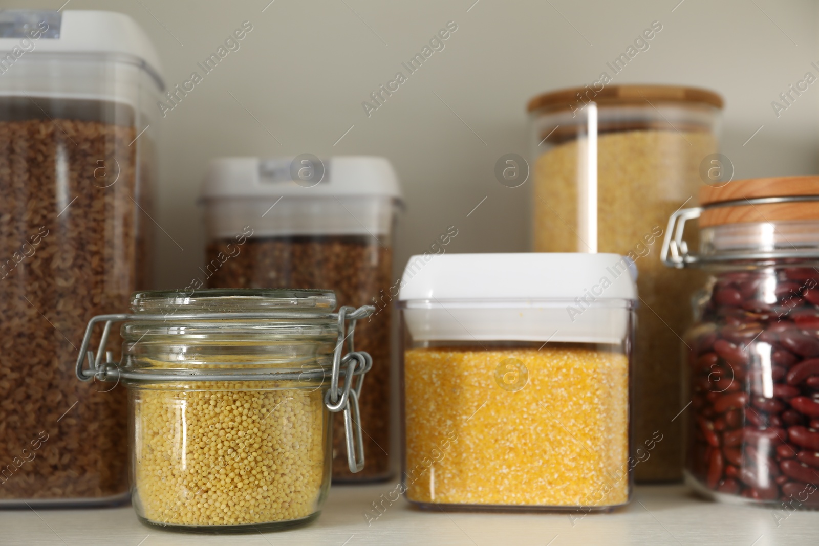 Photo of Different types of cereals and legumes in containers on white table, closeup