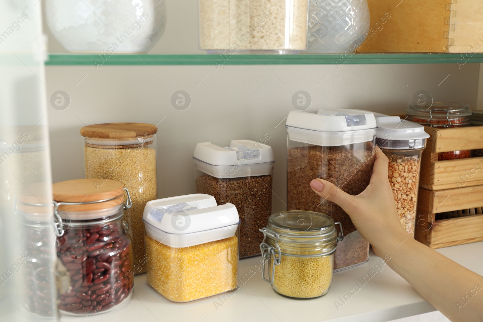 Photo of Woman with containers of different cereals and legumes in kitchen, closeup