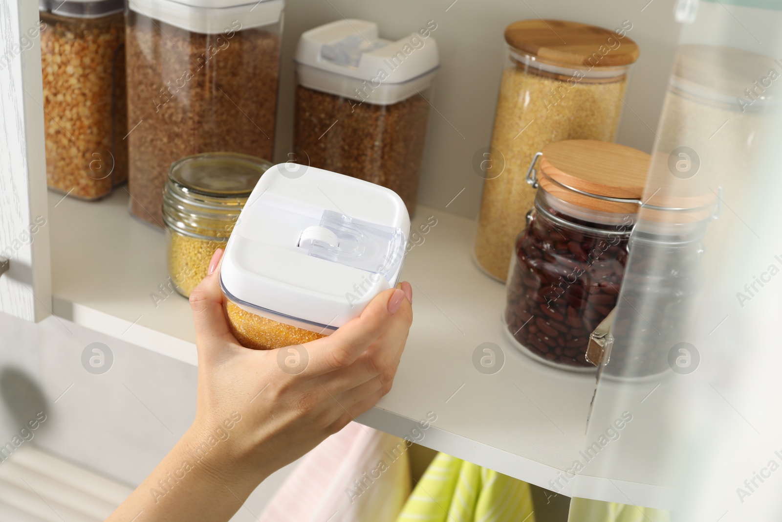 Photo of Woman with containers of different cereals and legumes in kitchen, closeup