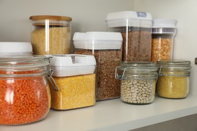 Photo of Different types of cereals and legumes in containers on shelf