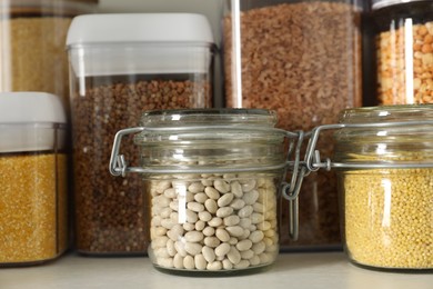 Photo of Different types of cereals and legumes in containers on white table, closeup