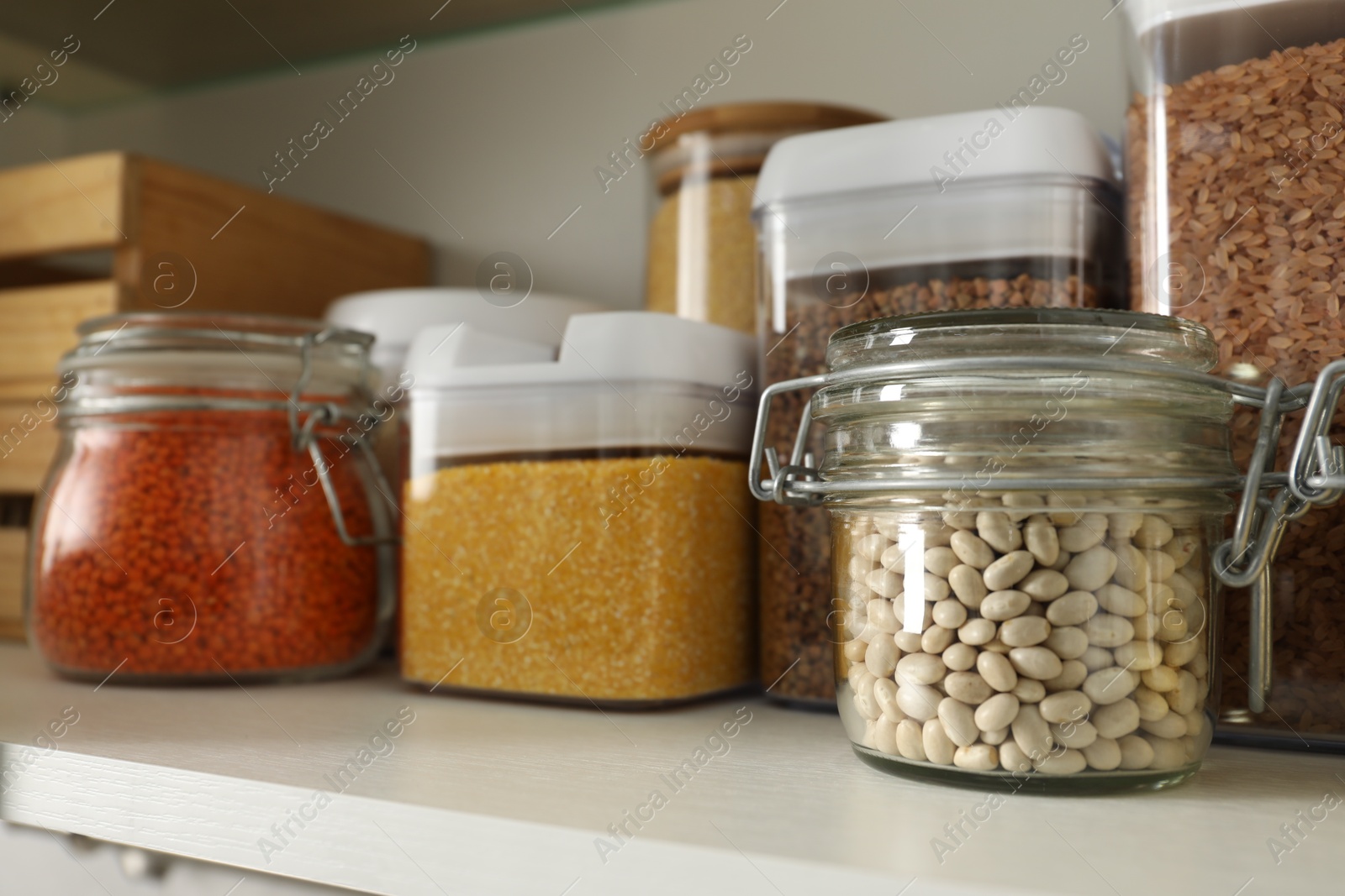 Photo of Different types of cereals and legumes in containers on shelf