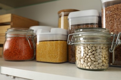 Photo of Different types of cereals and legumes in containers on shelf