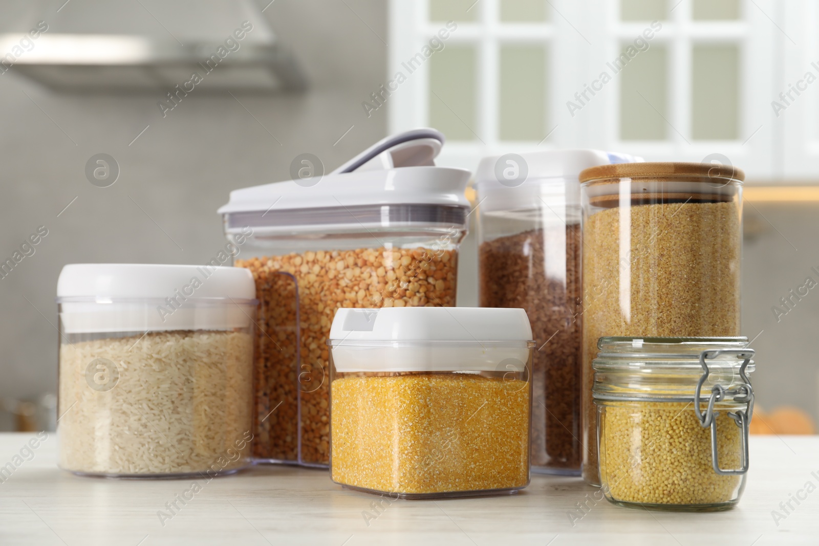 Photo of Different types of cereals and legumes in containers on white wooden table in kitchen