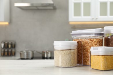 Different types of cereals and legumes in containers on white wooden table in kitchen, space for text