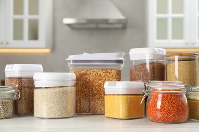 Photo of Different types of cereals and legumes in containers on white wooden table in kitchen