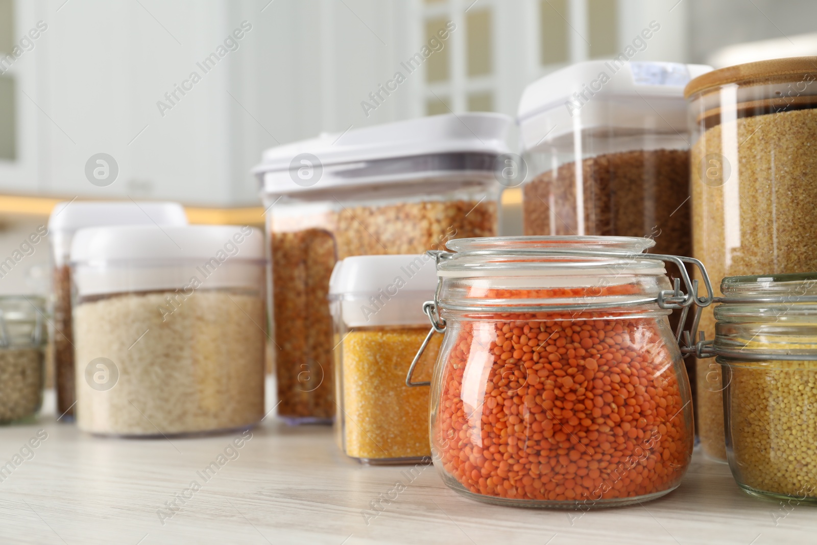 Photo of Different types of cereals and legumes in containers on white wooden table in kitchen, closeup