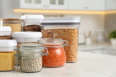 Different types of cereals and legumes in containers on white wooden table in kitchen, closeup