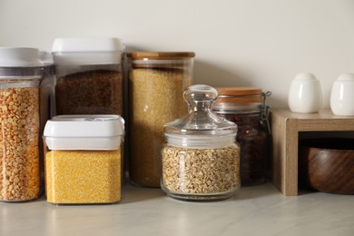 Different types of cereals and legumes in containers on light marble table