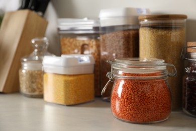 Photo of Different types of cereals and legumes in containers on light table, closeup