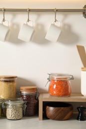 Photo of Different types of cereals and legumes in containers on light marble table in kitchen