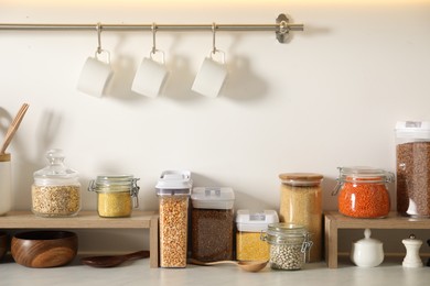 Photo of Different types of cereals and legumes in containers on light marble table in kitchen