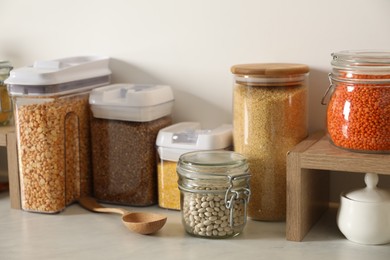 Photo of Different types of cereals and legumes in containers on light marble table in kitchen