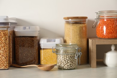 Photo of Different types of cereals and legumes in containers on light marble table in kitchen