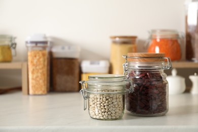 Photo of Different types of legumes in containers on light marble table. Space for text